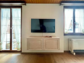 Ein Wohnzimmer mit einem an der Wand befestigten Flachbildfernseher, einem Holzschrank darunter und einer Schiebeglastür links.