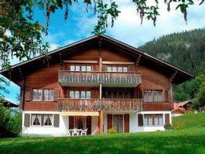 Een houten chalet met twee verdiepingen, een balkon en een veranda, met een berg op de achtergrond.