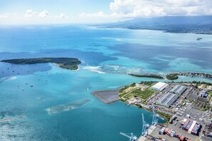 Vista aerea di una zona costiera con un porto turistico, edifici industriali e una grande nave cargo attraccata.