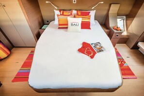 Ein kleines, helles Schlafzimmer mit Bett, Kissen, einem Nachttisch, einem Fenster und einem Tisch mit einer Zeitschrift.