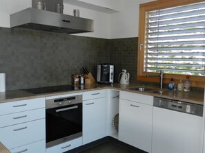 Een moderne keuken met witte kastjes, een ingebouwde oven, een koffieapparaat en een raam met zonwering.