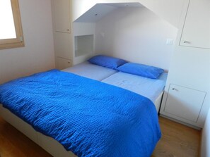 Een slaapkamer met een bed, een blauwe spreidek, een witte matras en een schuine hemel.