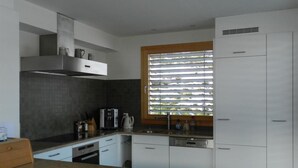 Eine moderne Küche mit weißen Schränken, einem Backofen und einem Fenster mit Jalousien.