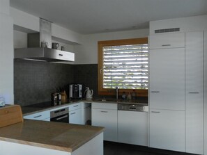 A modern kitchen with white cabinetry, a built-in oven, and a window with blinds. - Gletscherblick, Chalet Appartement/Fewo, Dusche oder Bad, WC 10-Bettwohnung by Interhome (Zweisimmen)