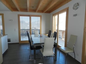 A dining area with a table and chairs, large windows, and a wooden ceiling. - Gletscherblick, Chalet Appartement/Fewo, Dusche oder Bad, WC 10-Bettwohnung by Interhome (Zweisimmen)