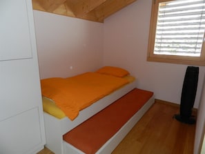 A small, single-bed room with a sloped ceiling and a window with blinds. - Gletscherblick, Chalet Appartement/Fewo, Dusche oder Bad, WC 10-Bettwohnung by Interhome (Zweisimmen)