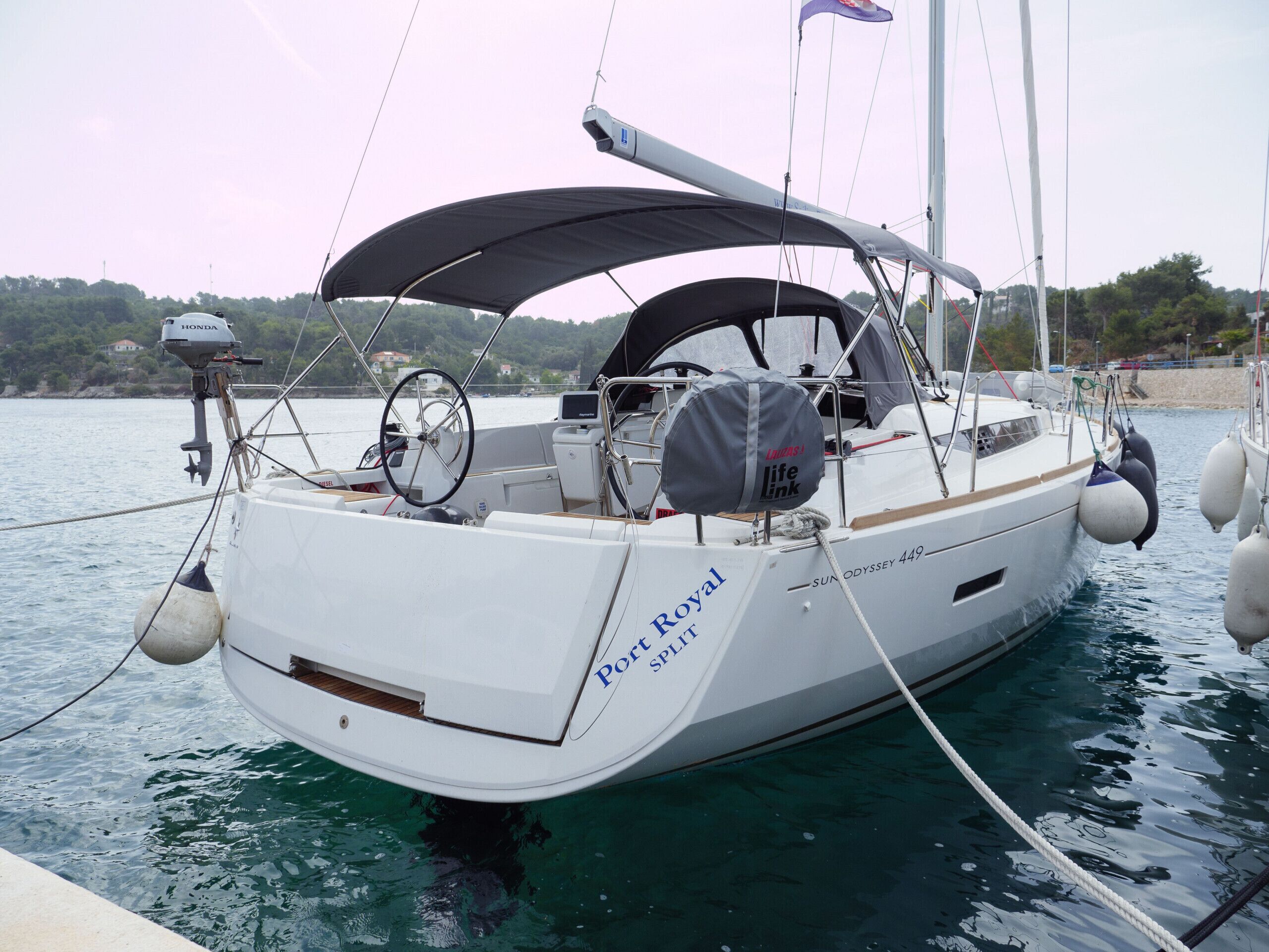 Een zeilboot genaamd 'Port Royal Splendid' ligt afgemeerd in een jachthaven met uitzicht op het water en de verre kustlijn.