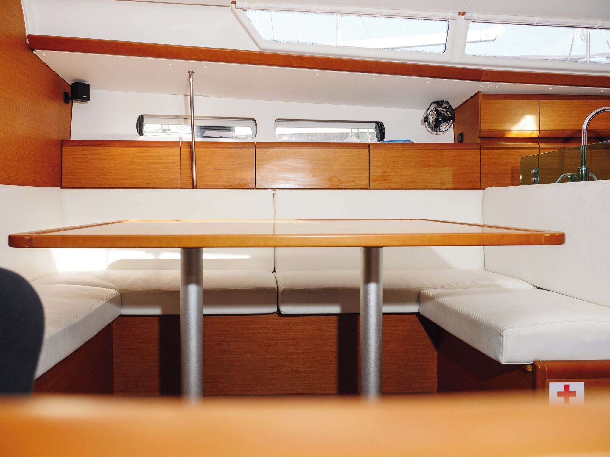 Interior de embarcación con mesa de madera, asientos acolchados y pequeña cocina.