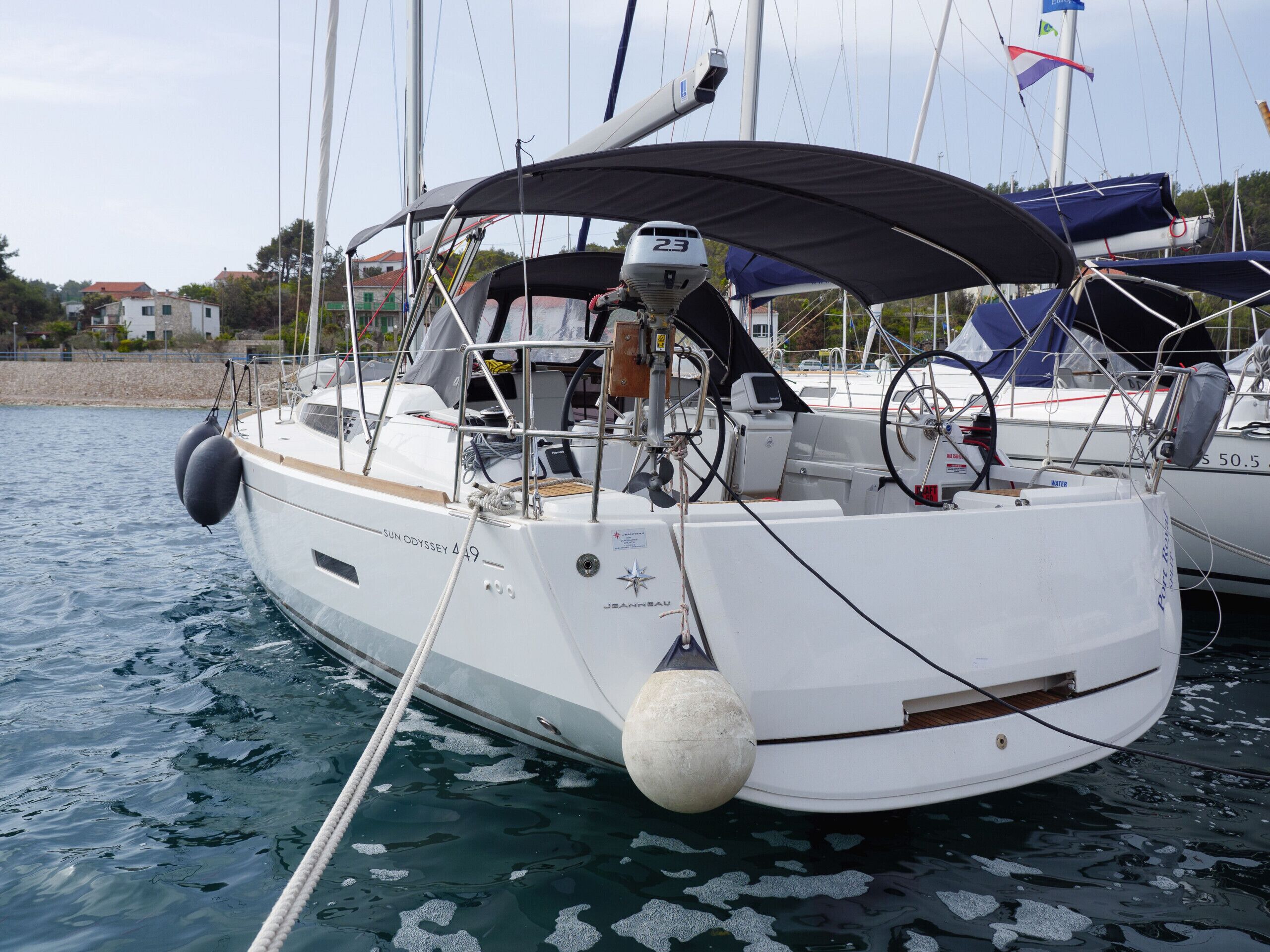 Een zeilboot afgemeerd in een jachthaven, met een afgesloten kuip, stuurwiel en diverse navigatieapparatuur.