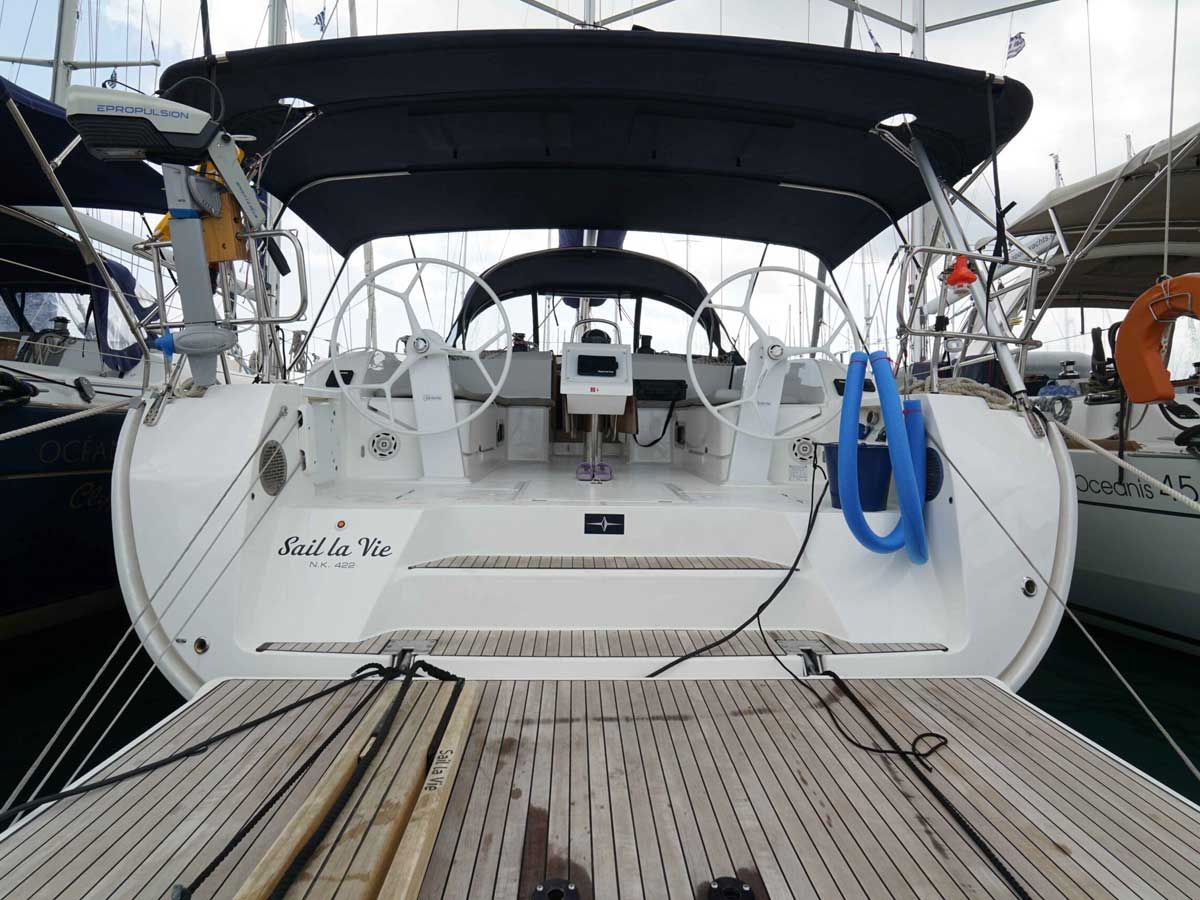 Dek van een boot met een stuurwiel, een reddingsboei, en de naam 'Sail la Vie' op de zijkant.