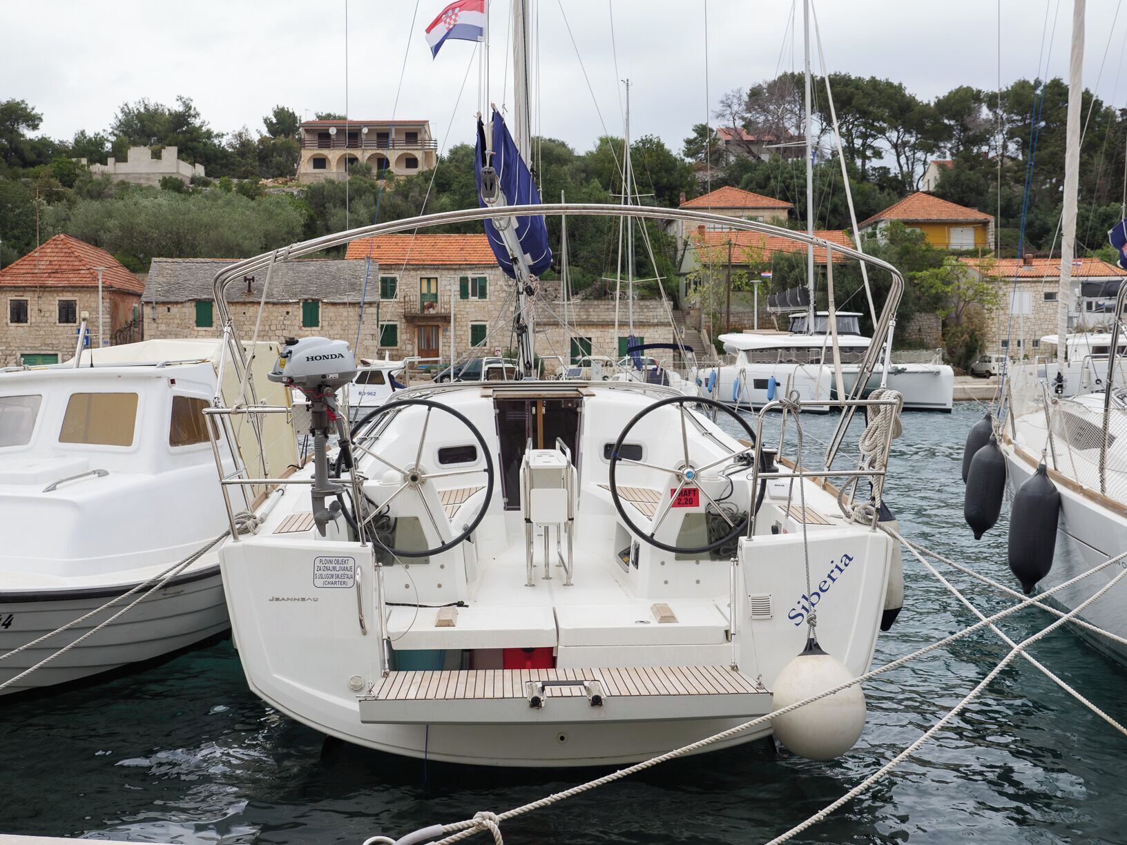Un barco amarrado en un puerto deportivo, con una bandera, un timón y una cabina.