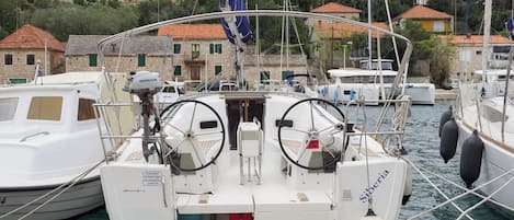 Un barco amarrado en un puerto deportivo, con una bandera, un timón y una cabina.