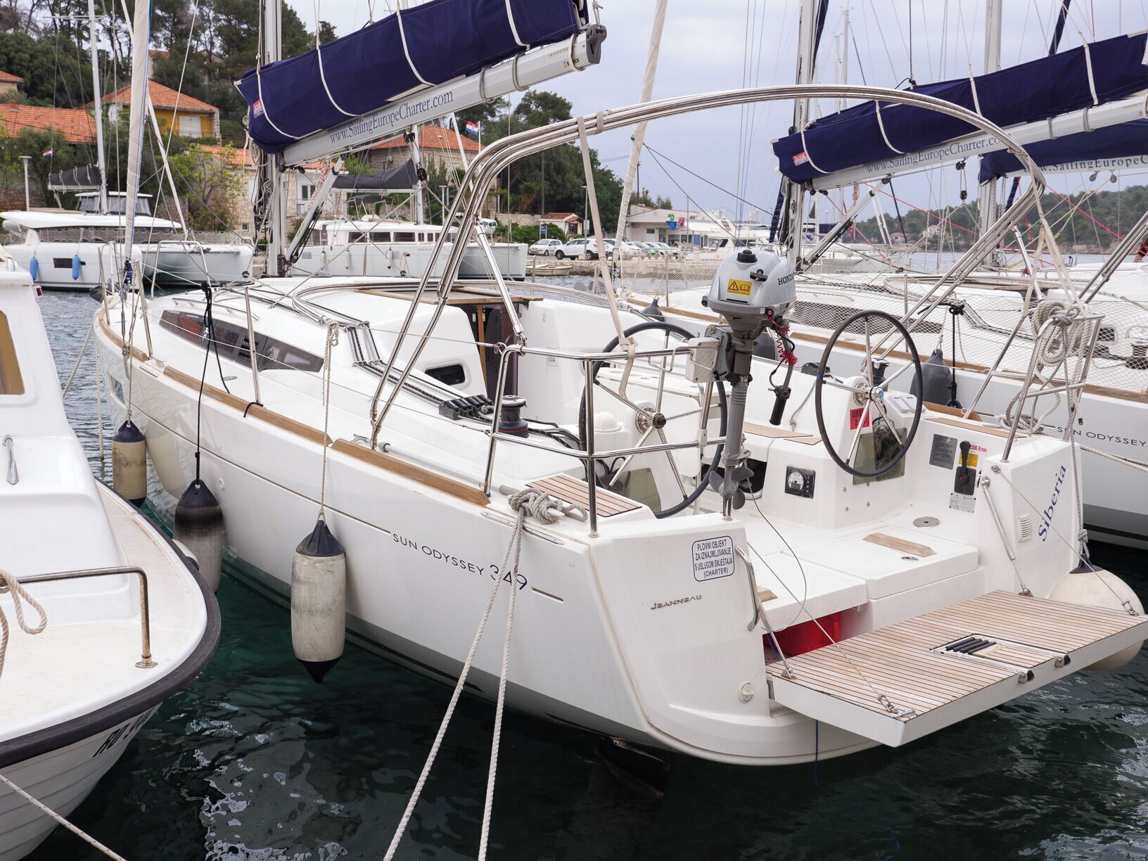 Un yate blanco amarrado en un puerto deportivo, con cabina, pequeña cubierta y un flotador.