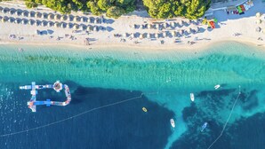 Ovenudblik over en strand med klart turkis vand, en mole og flere både.