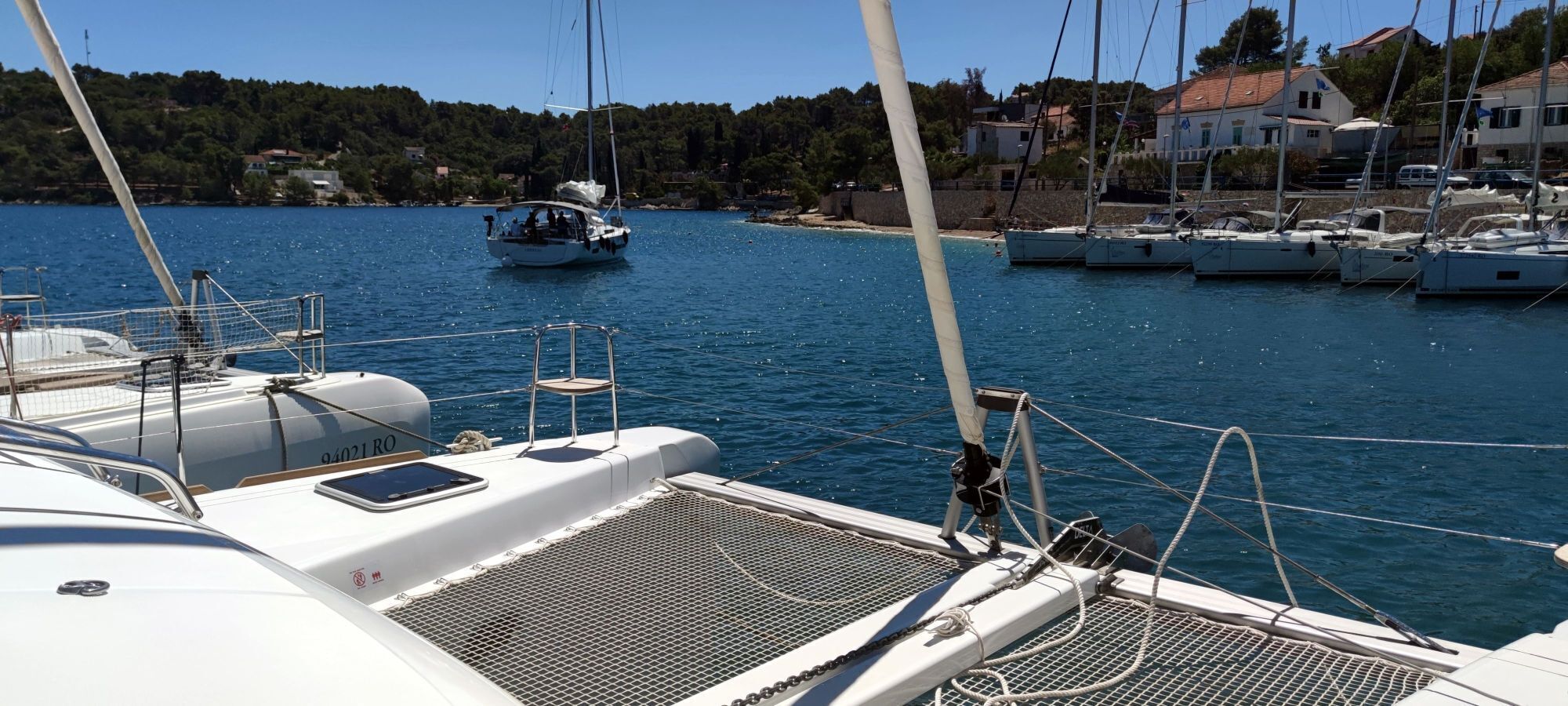 A marina with boats docked, a person standing on a boat, and houses in the background.
