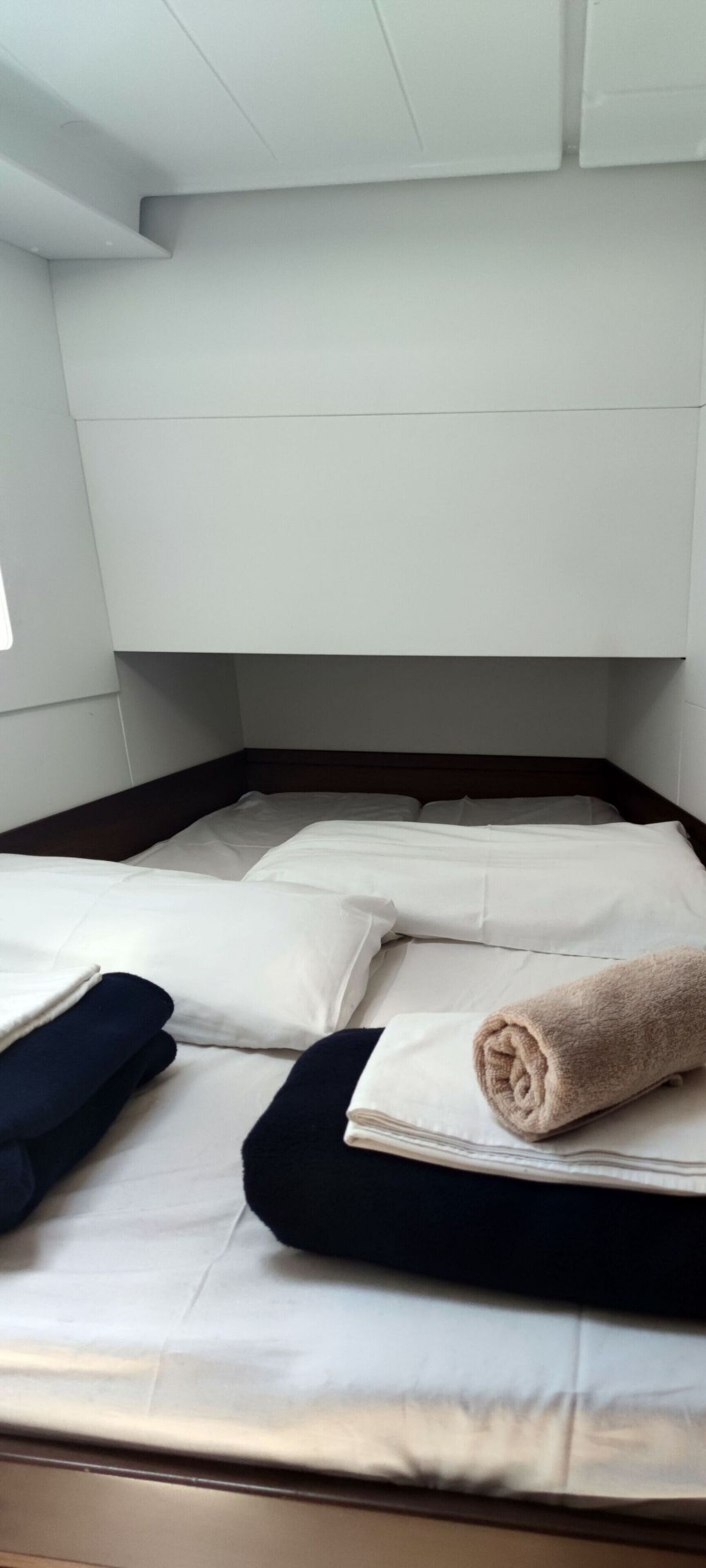 A bed with white bedding, a rolled towel, and dark pillows.