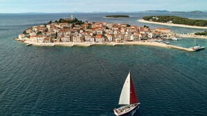 Oversigtsbillede af en kystby med en markant ø, en sejlbåd og krystalklart hav.