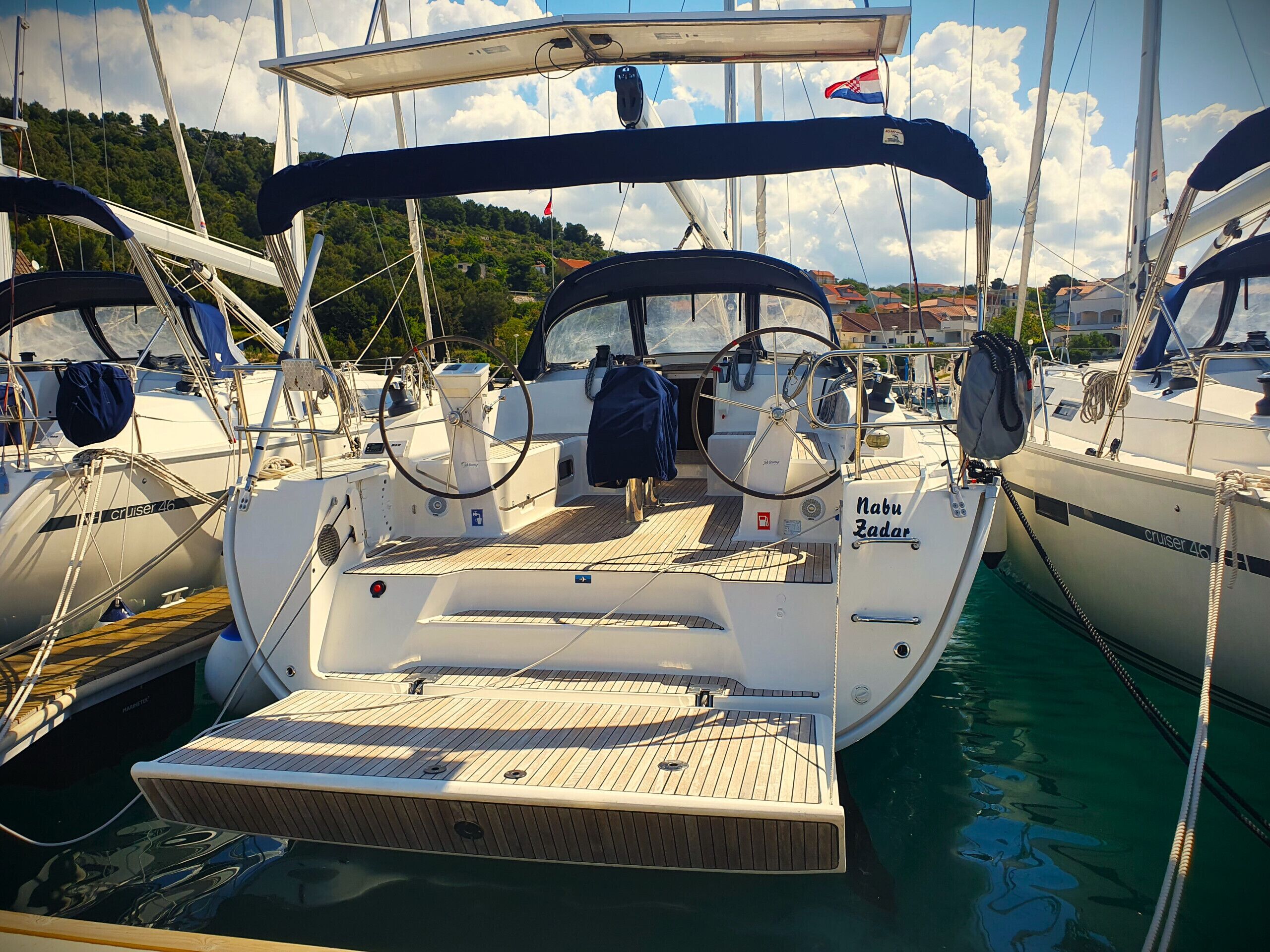 A marina with boats docked, including a boat named 'Nabu Zadar' with a wooden deck and a steering wheel.