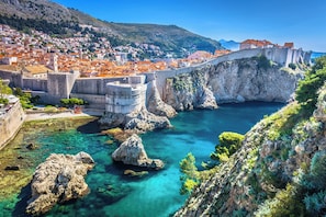 Eine Küstenstadt mit einer historischen Steinbrücke, klarem türkisblauem Wasser und einem bergigem Hintergrund.