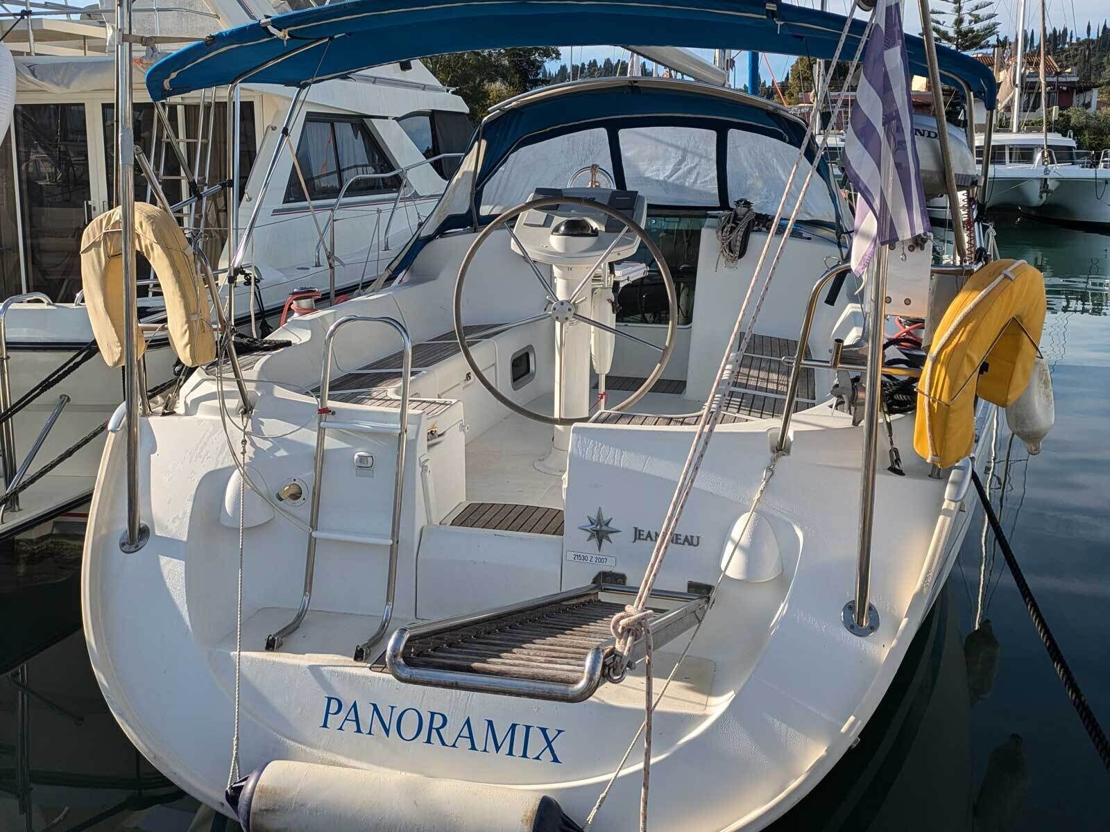 A boat named 'PANORAMIX' docked at a marina with a white hull, blue canopy, and visible deck equipment.