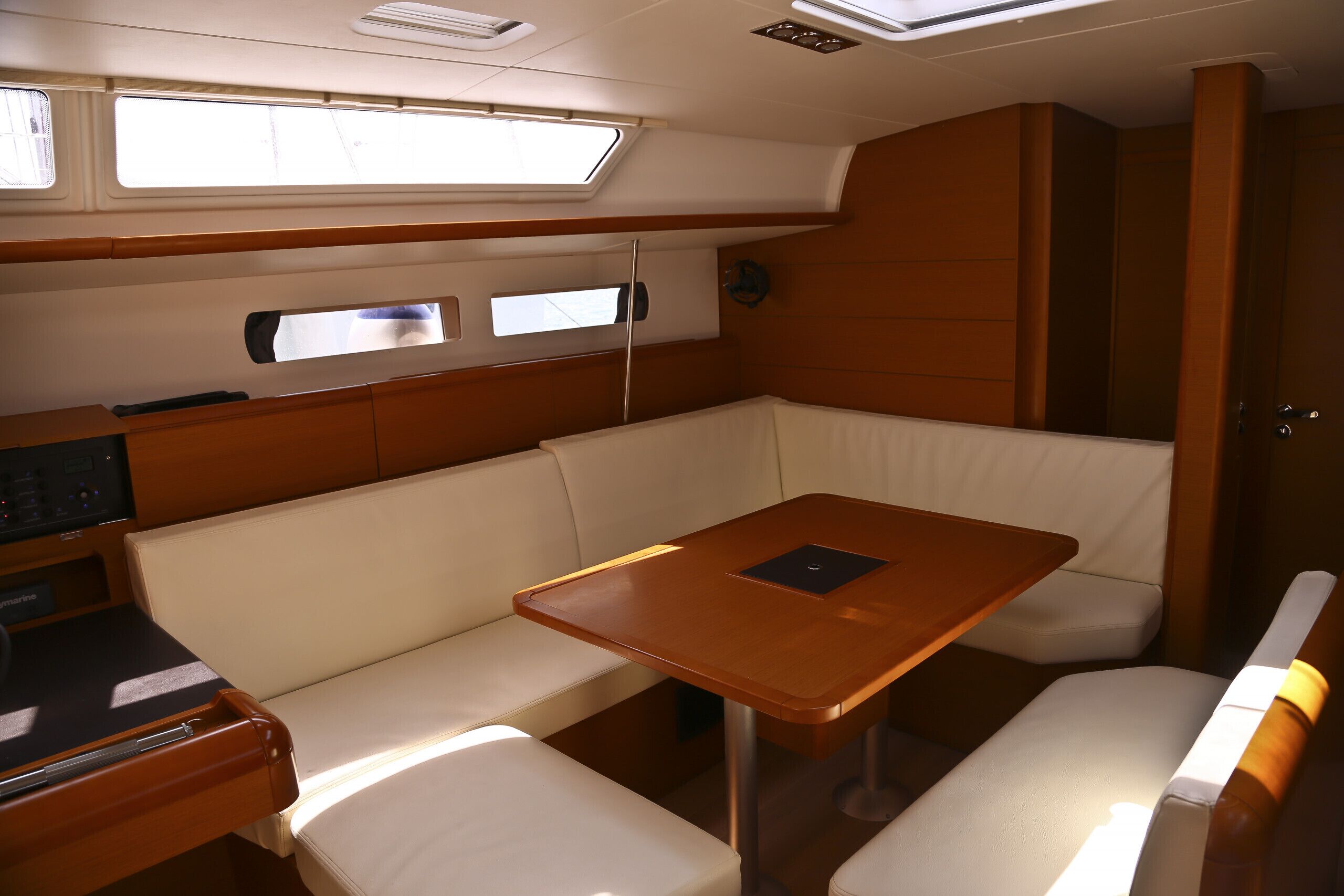 A cabin with a wooden table and cushioned seating, a control panel, and windows.