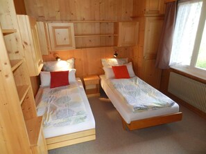 Quarto de madeira com duas camas de solteiro, cada uma com uma almofada e uma luminária de cabeceira.