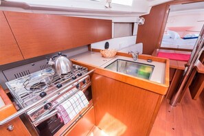 A compact kitchen with a stove, sink, and wooden cabinets. - Sun-Kissed Sailing Adventure in Split, Croatia (Split)