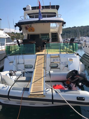 Eine Yacht namens 'ROYAL SPLIT' liegt in einer Marina festgemacht, mit Holzdeck, Sitzgelegenheit und einem sichtbaren Rettungsring.