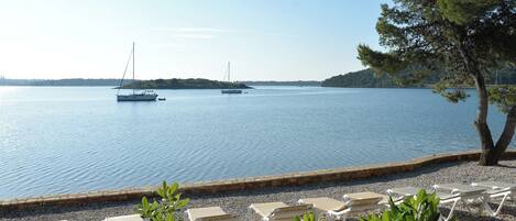 A calm lake with boats, a pebble beach, and lounge chairs.