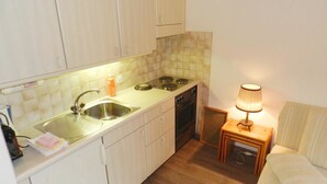 Una cocina compacta con lavamanos, estufa y una pequeña mesa con lámpara.