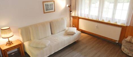 Quarto com sofá, luminária, radiador e janela com cortinas.
