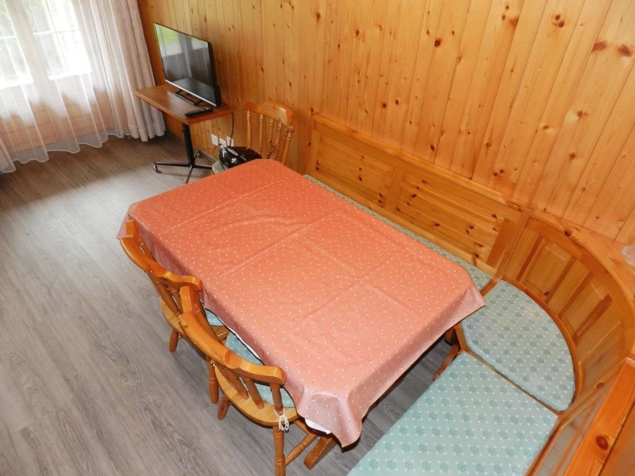 A room with a wooden table, chairs, a television, and a window with curtains.