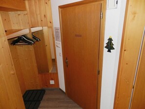 Een smalle gang met houten wanden, een deur, een kapstok en een kleine kerstversiering.