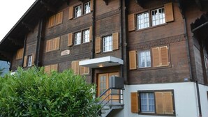 Un edificio de varios pisos con persianas de madera, una escalera y un pequeño jardín.