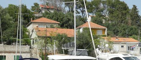 Un port esportiu amb vaixells amarrats, un edifici de pedra amb teulada vermella i arbres al fons.