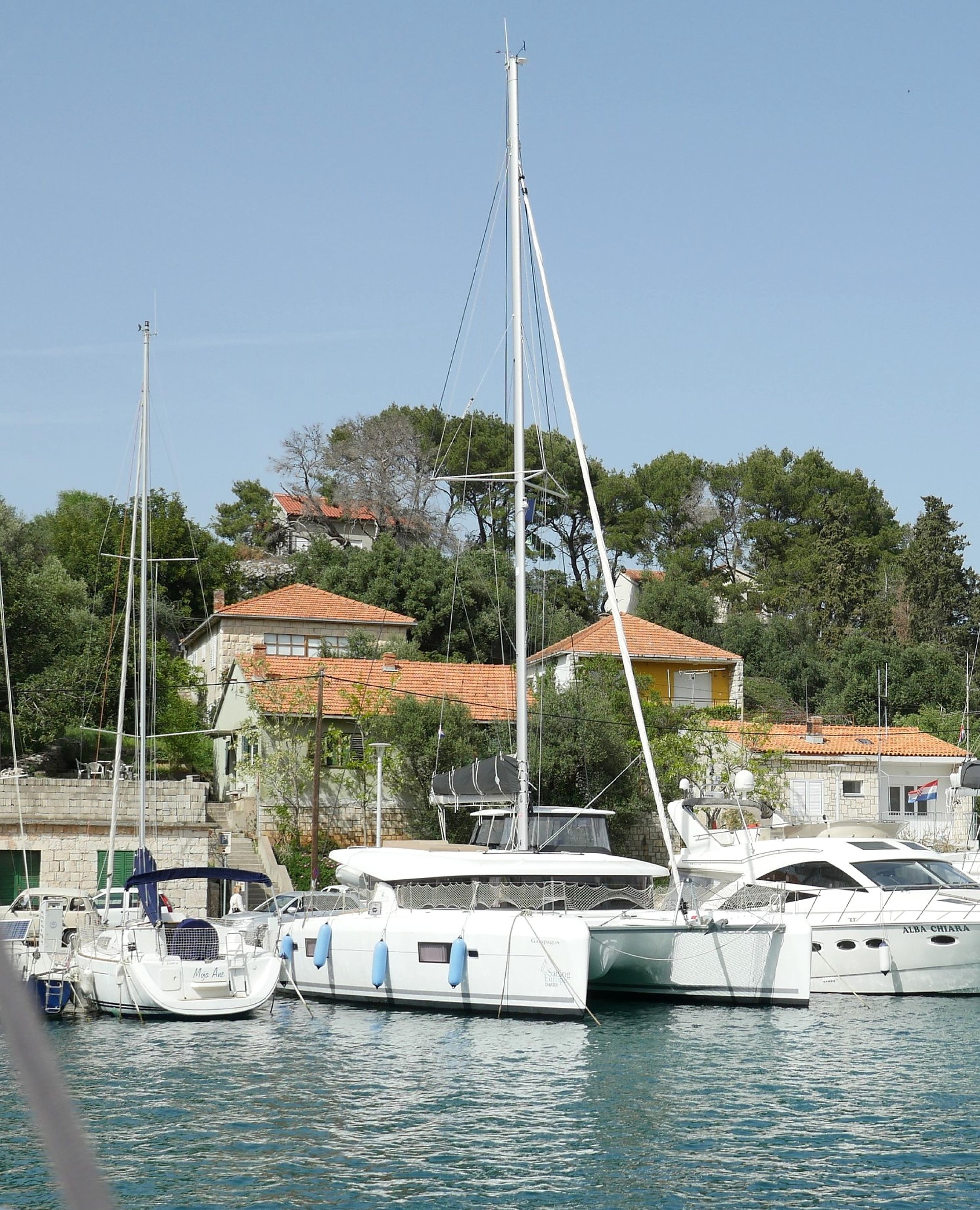 A marina with several yachts docked, surrounded by residential buildings with red-tiled roofs.