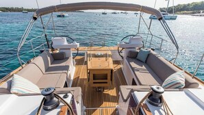 Ein Bootsdeck mit überdachter Sitzecke, einem zentralen Tisch und Blick auf das Wasser sowie weitere Boote.