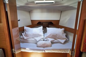 Un lit compact avec une literie blanche, situé dans une cabane aux murs en bois et éclairée par un luminaire au plafond.