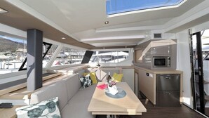 Interni di uno yacht con zona pranzo, cucina e vista sul porto turistico.