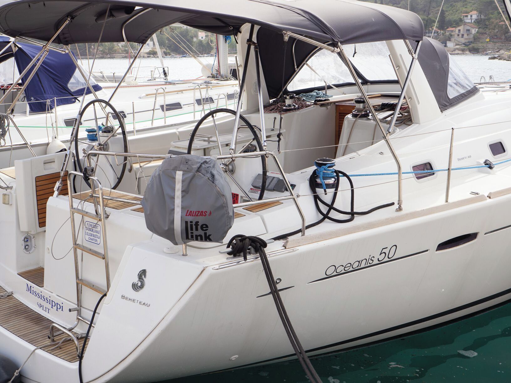 Een witte jacht genaamd 'Oceanis 50' met een afgesloten cockpit, een reddingsboei en een tas van 'LALIZAS'.