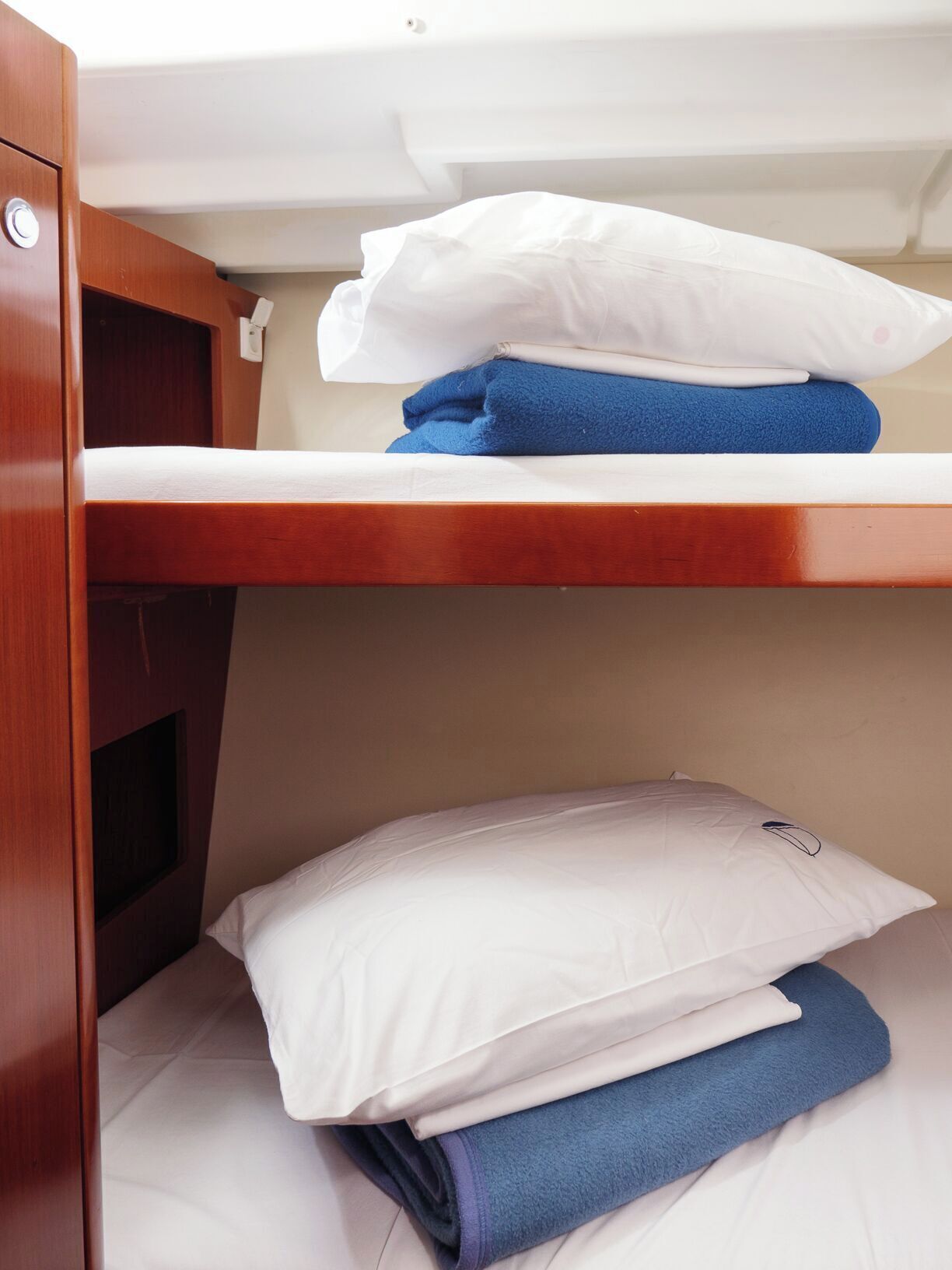 Una cama litera con ropa de cama blanca y azul, un cabecero de madera y un pequeño compartimento de almacenamiento.