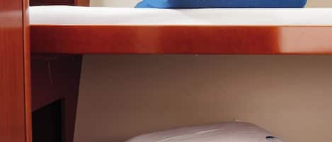 Una cama litera con ropa de cama blanca y azul, un cabecero de madera y un pequeño compartimento de almacenamiento.
