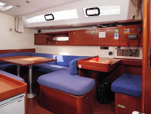 A compact cabin with a wooden table, blue cushioned seating, a small kitchenette, and a control panel with various buttons and a phone. - Sun-Kissed Sailing Adventure in Split, Croatia (Rogac)