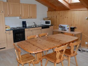 A kitchen with wooden cabinets, a microwave, a coffee maker, and a dining table with chairs. - Jacqueline 24 Appartement/Fewo, Dusche oder Bad, WC 5-Bettwohnung by Interhome (Gstaad)