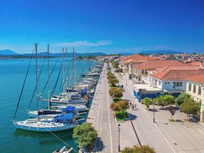 A marina with boats docked along a waterfront promenade, lined with buildings and trees.