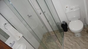 A bathroom with a glass shower enclosure, a toilet, and a towel rack. - Hotel Niro (Montenegro)