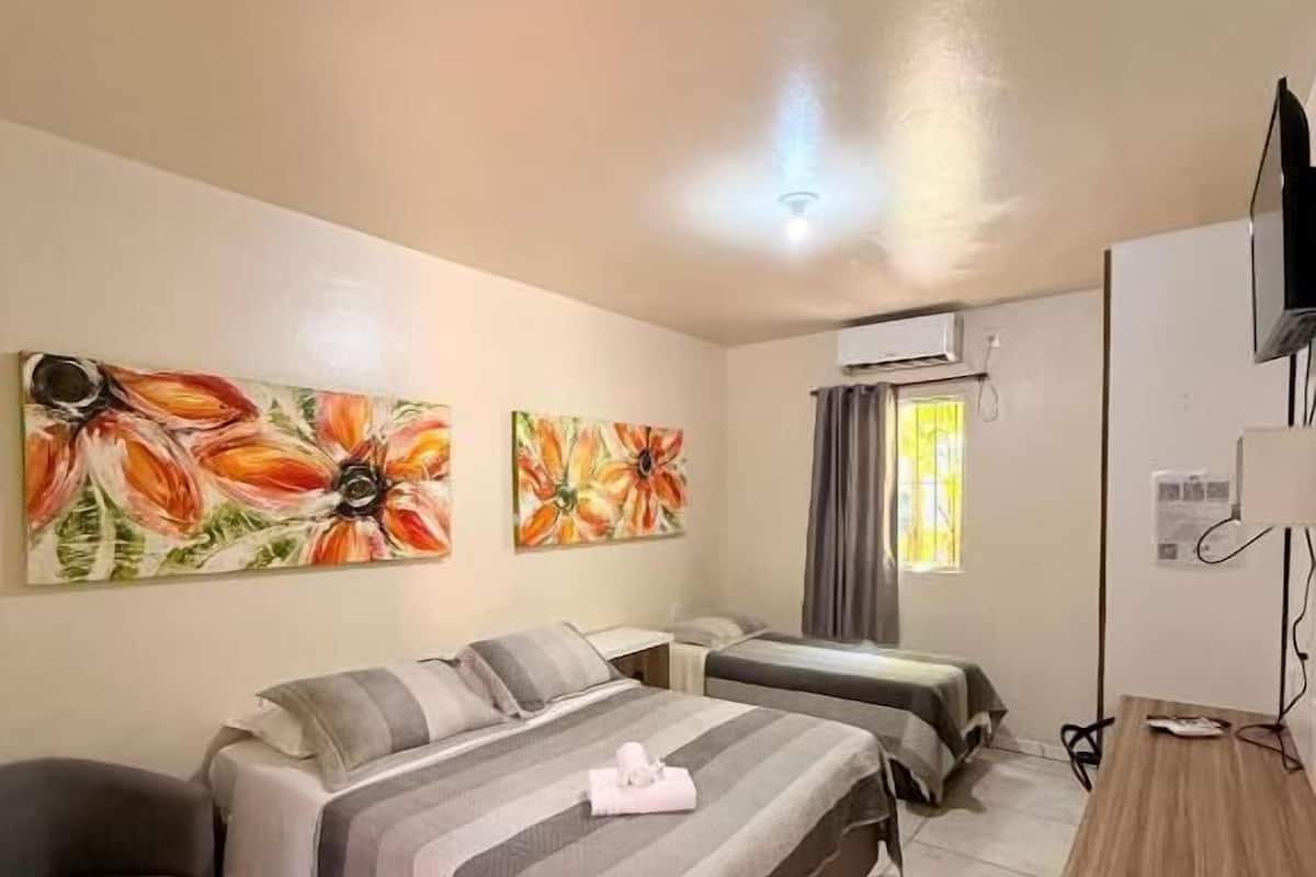 A hotel room with a bed, a desk, a chair, and two paintings on the wall.