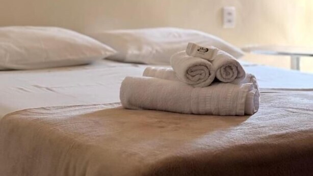 A neatly made bed with rolled towels, a white pillow, and a framed floral artwork on the wall. - Hotel Niro (Montenegro)