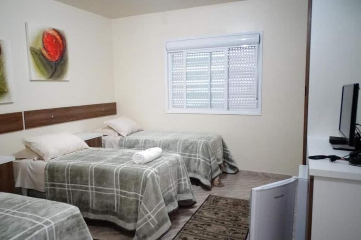 A room with two beds, a desk, a TV, and artwork on the wall.