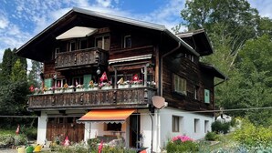 Eine zweistöckige Holzchalet mit Balkon, umgeben von üppigem Garten und einer Flagge.